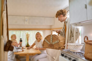 Happy family on the kitchen in trailer, summer camping. Couple with kids travel in camp car, motorhome interior on background. Campsite adventure, travelling lifestyle, vacation on rv vehicle