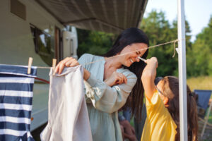 A mother with daughter hanging clothes by car outdoors in campsite, caravan family holiday trip.